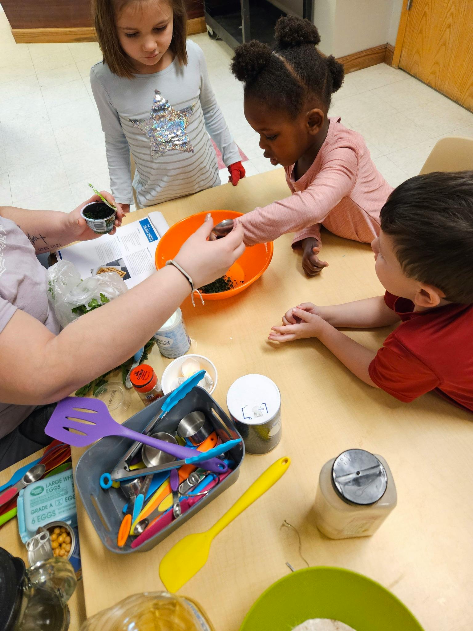 Adult and three children at a table with cooking ingredients and baking supplies