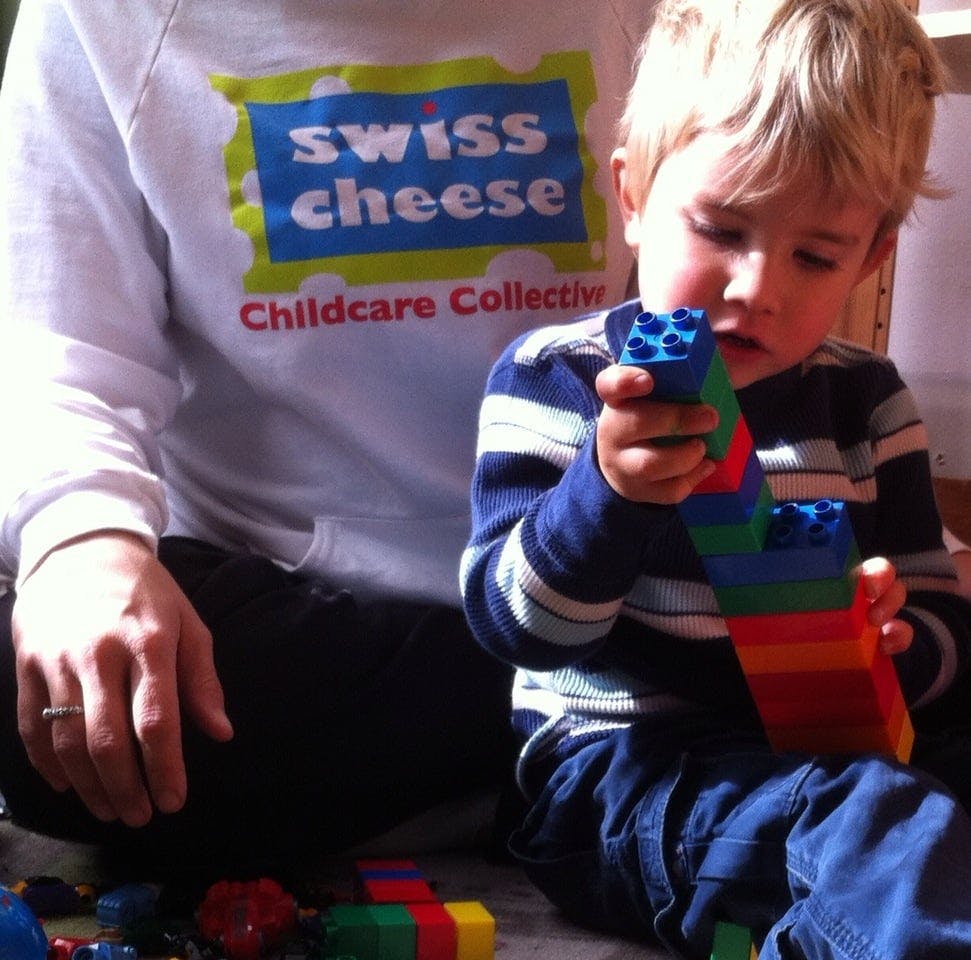 Child playing with colorful building blocks next to a person