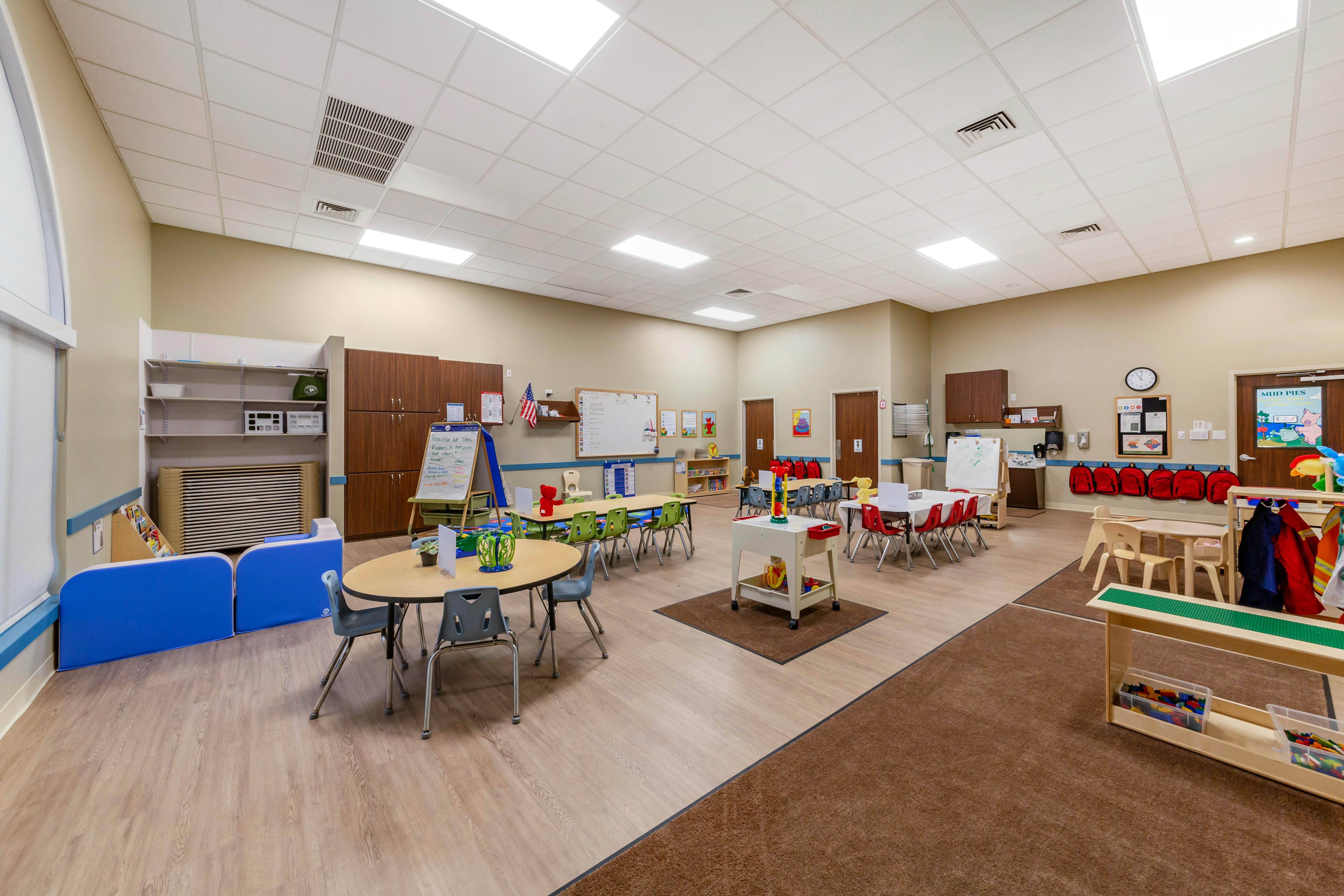 Classroom with child-sized tables and chairs, whiteboards, and storage cabinets