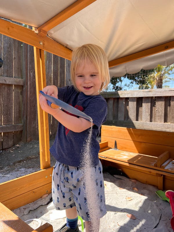 Child pouring sand from a blue shovel in a sandbox