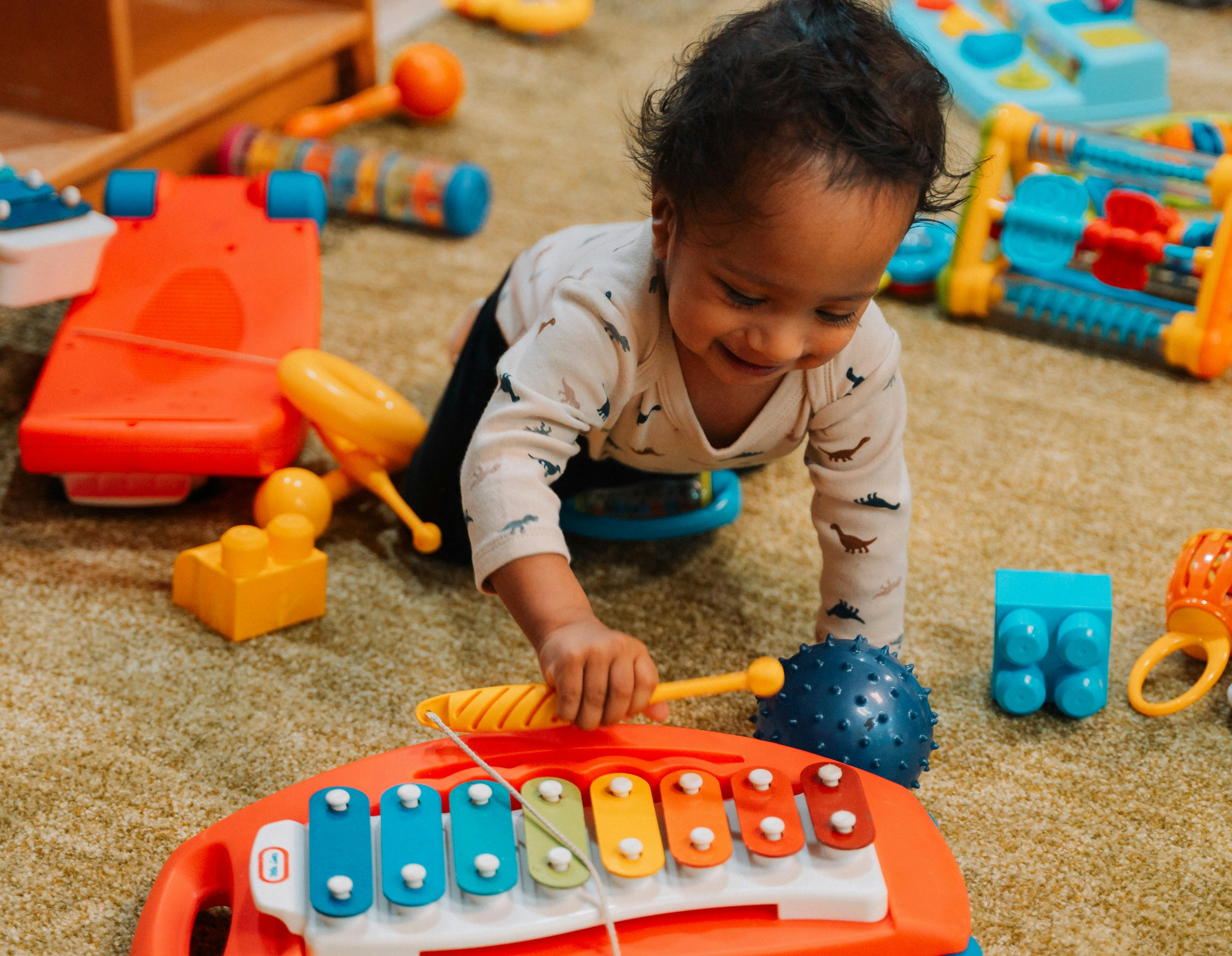 Child playing with a toy xylophone and mallet on a carpeted floor