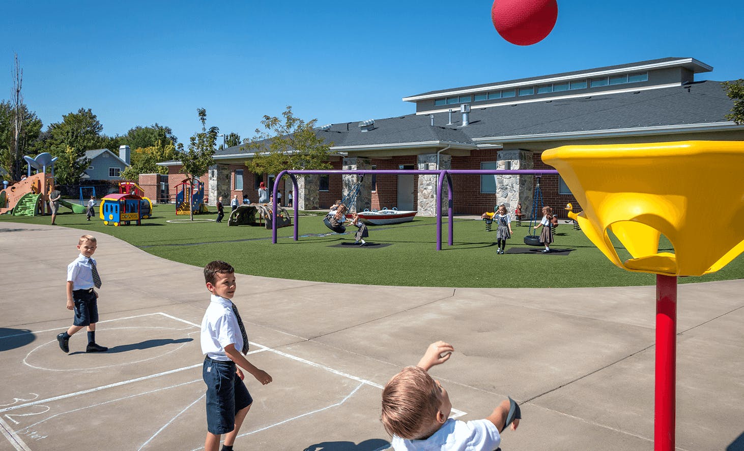 Children playing on a playground with a red ball in the air