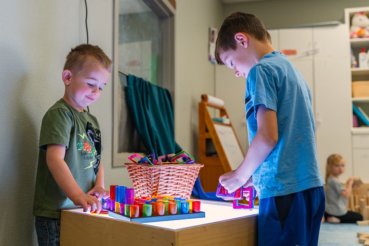 Two children playing with colorful blocks on a light table in a classroom