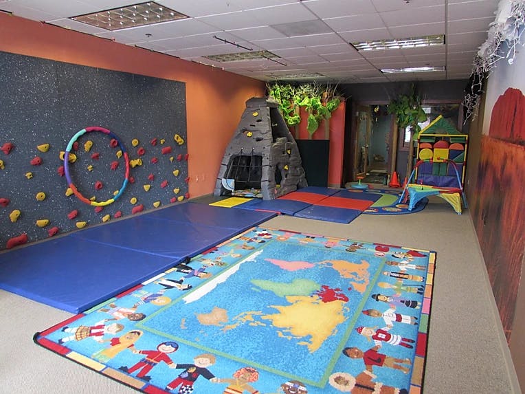 Indoor play area with a climbing wall, play structure, and world map rug