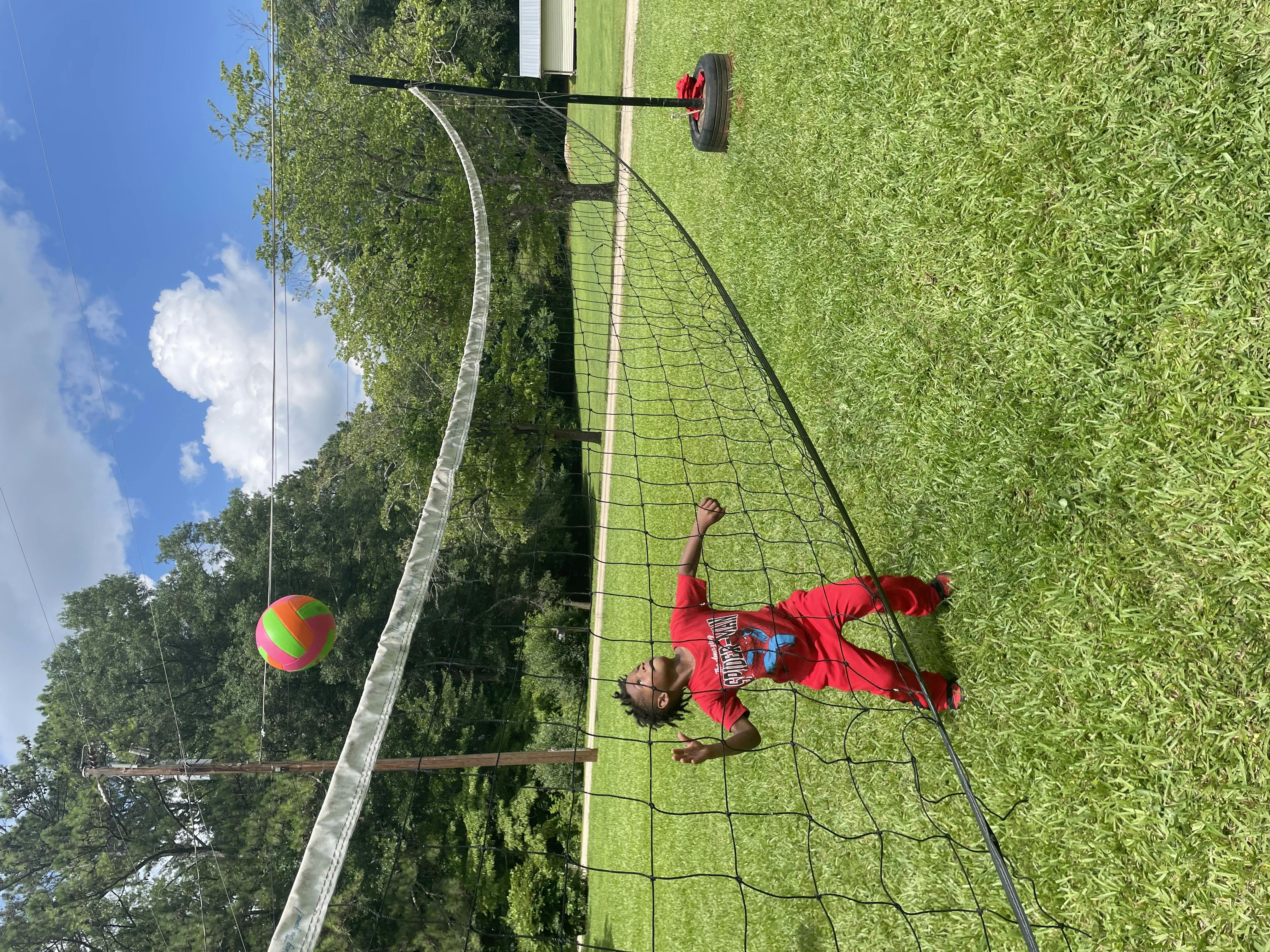 Child in red playing volleyball on a grassy court