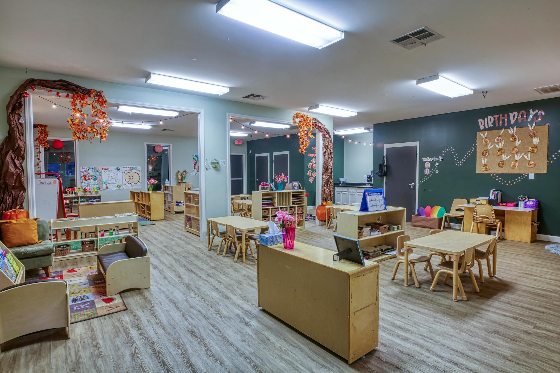 Classroom with small tables, chairs, shelving units, and a bulletin board that says "BIRTHDAYS"