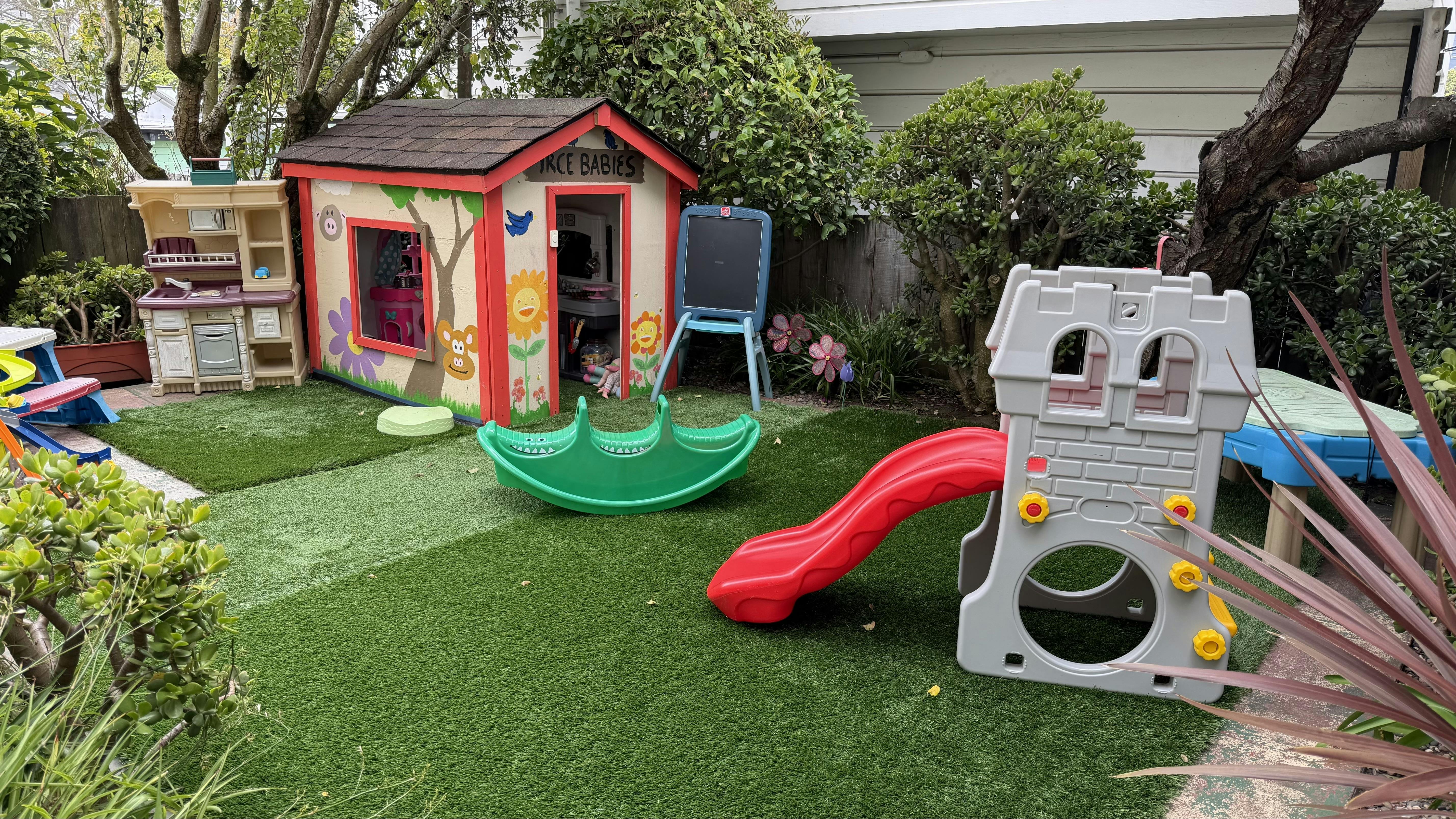 Childrens play area with plastic playhouse slide and rocker on artificial grass