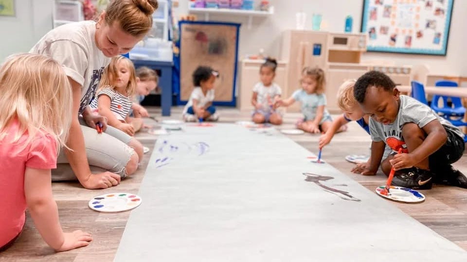 Adult and children painting on a large sheet of paper on the floor