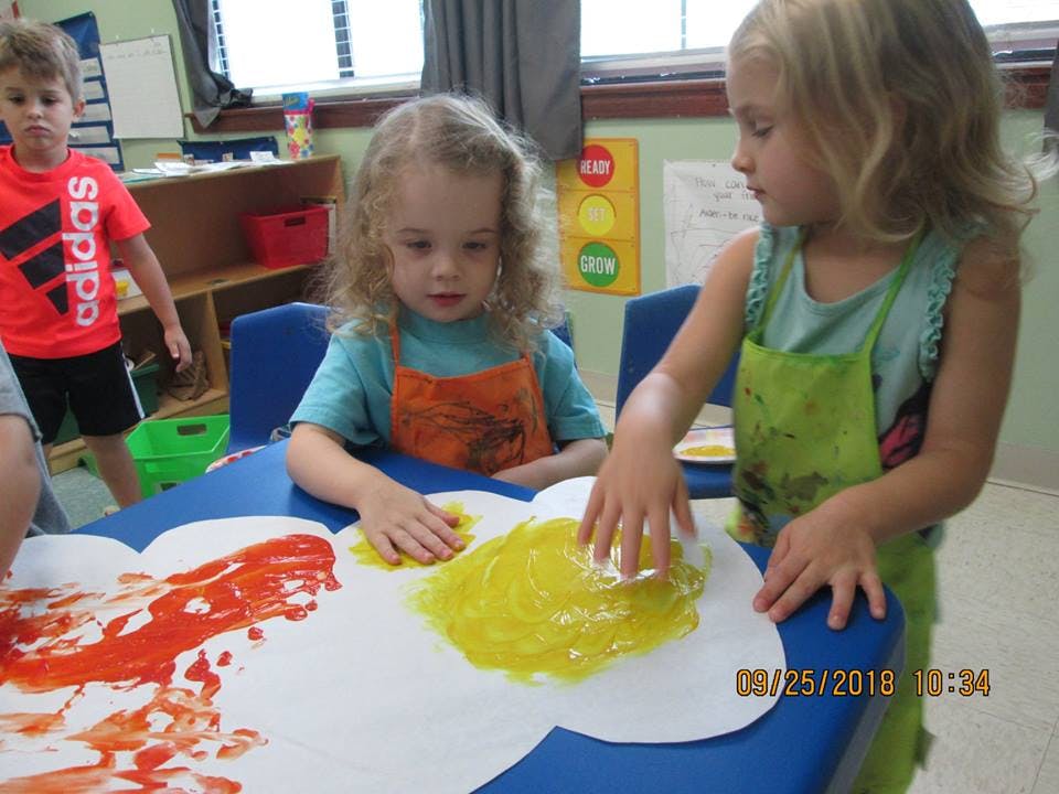 Two children finger painting at a table in a classroom