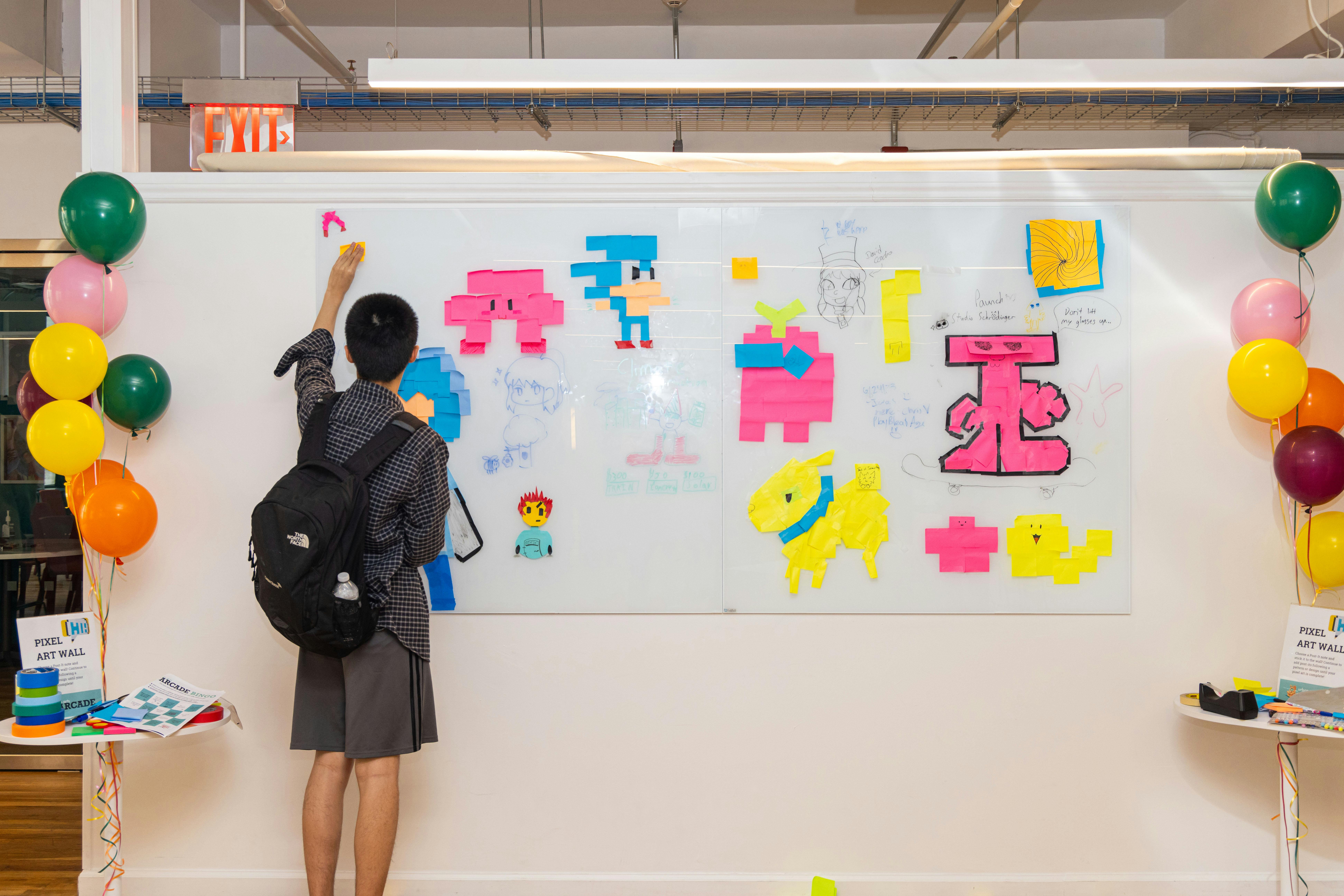 Person with backpack drawing on a whiteboard with colorful cutouts