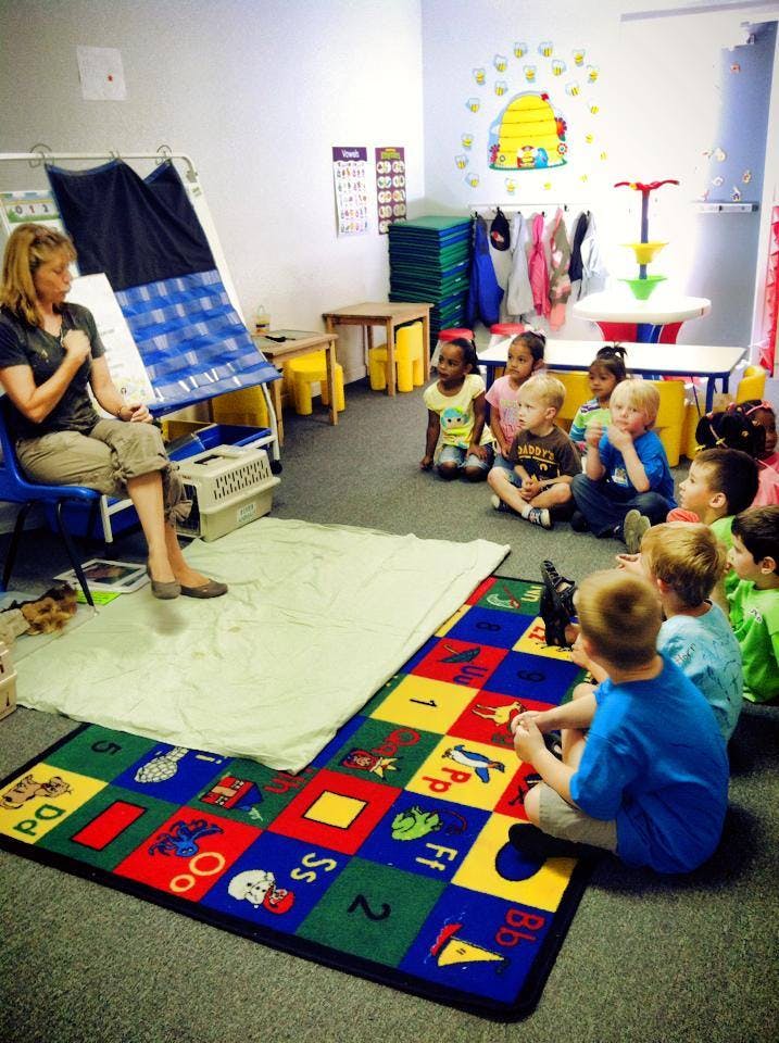 Adult sitting in a chair with children sitting on a rug in a classroom