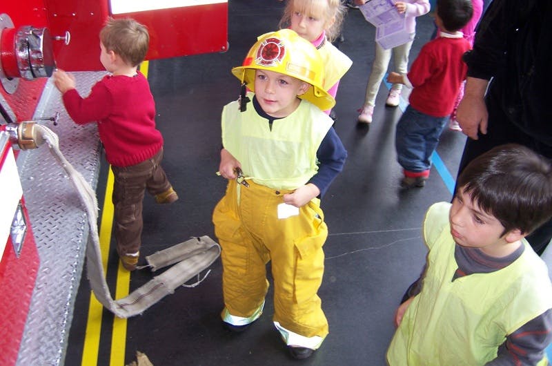 Children in firefighter costumes playing with a fire truck hose