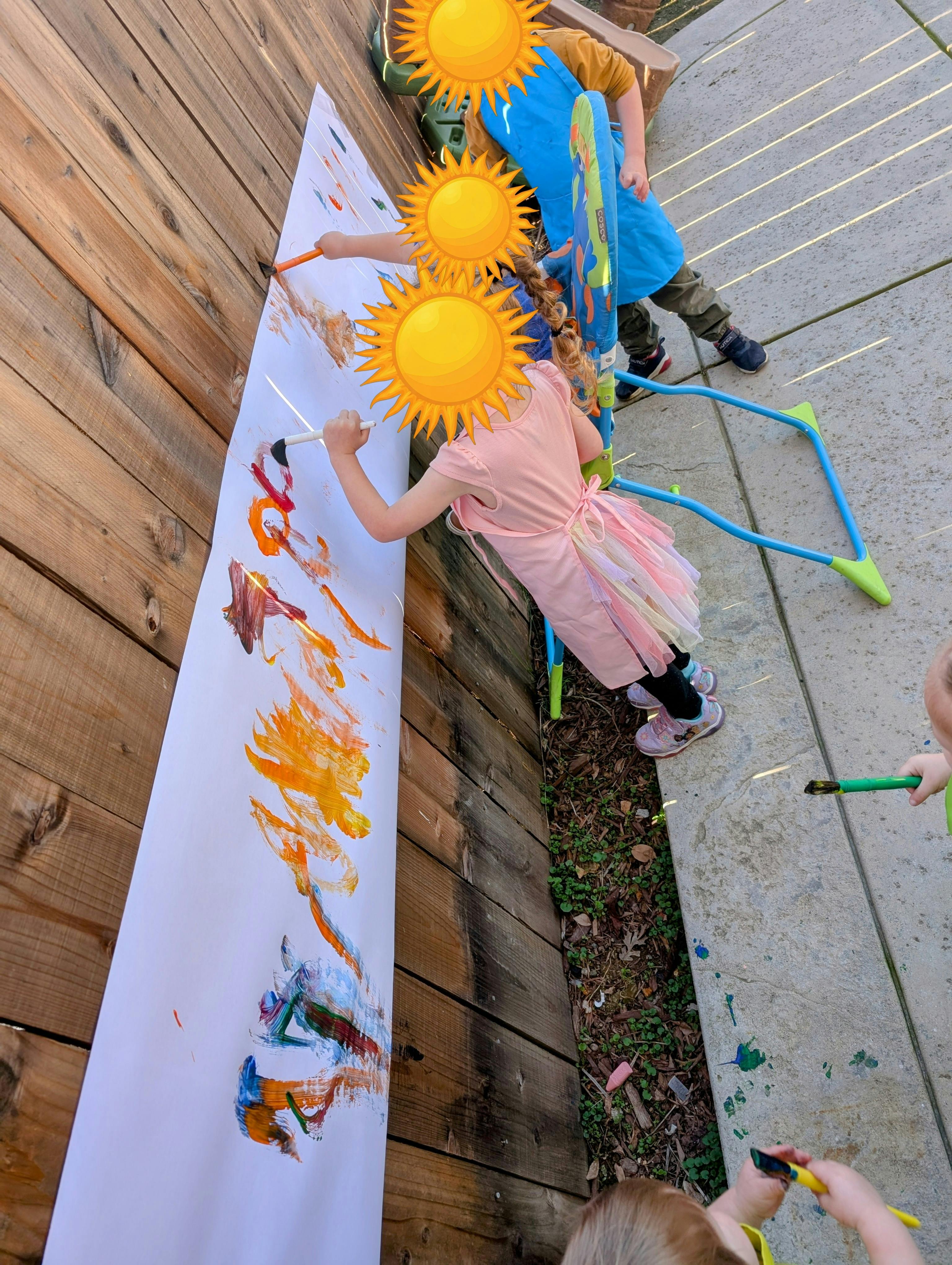 Children painting on a long sheet of paper outdoors