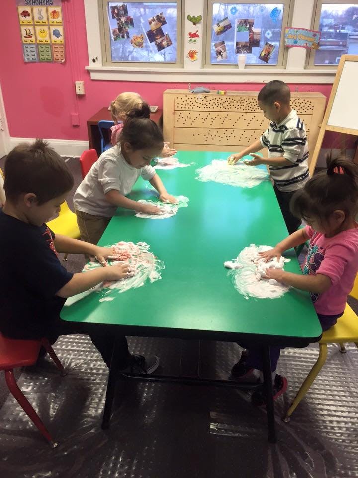 Children playing with shaving cream on a green table in a classroom