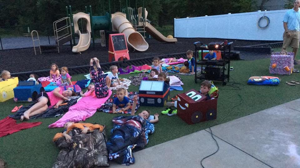 Children on blankets and in sleeping bags on grass near playground equipment
