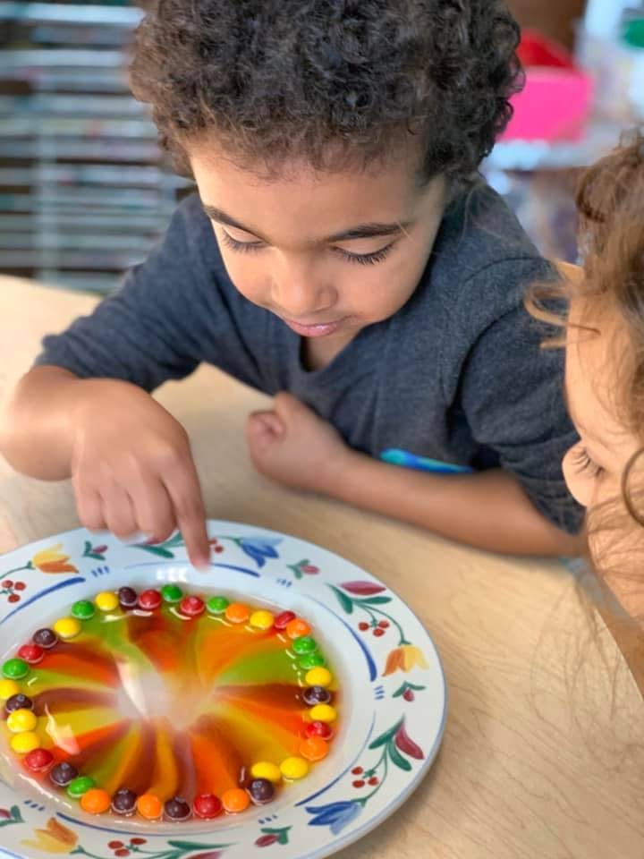 Child pointing at colorful candies dissolving in liquid on a plate