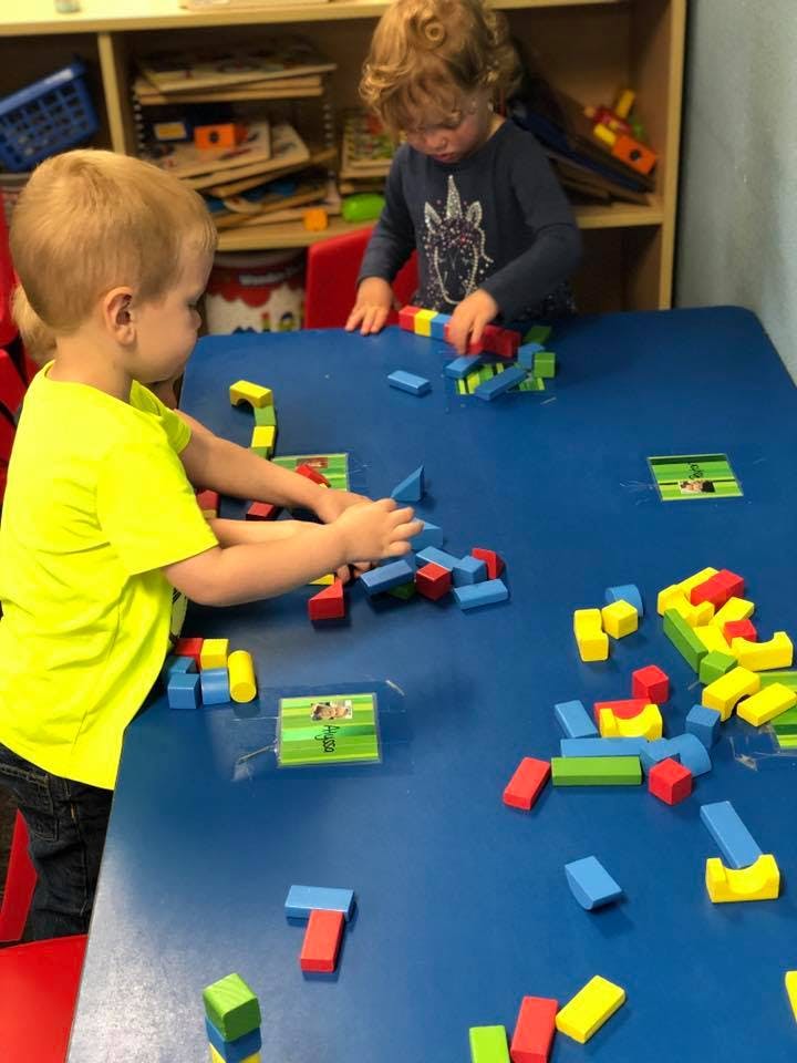 Two children playing with colorful building blocks on a blue table