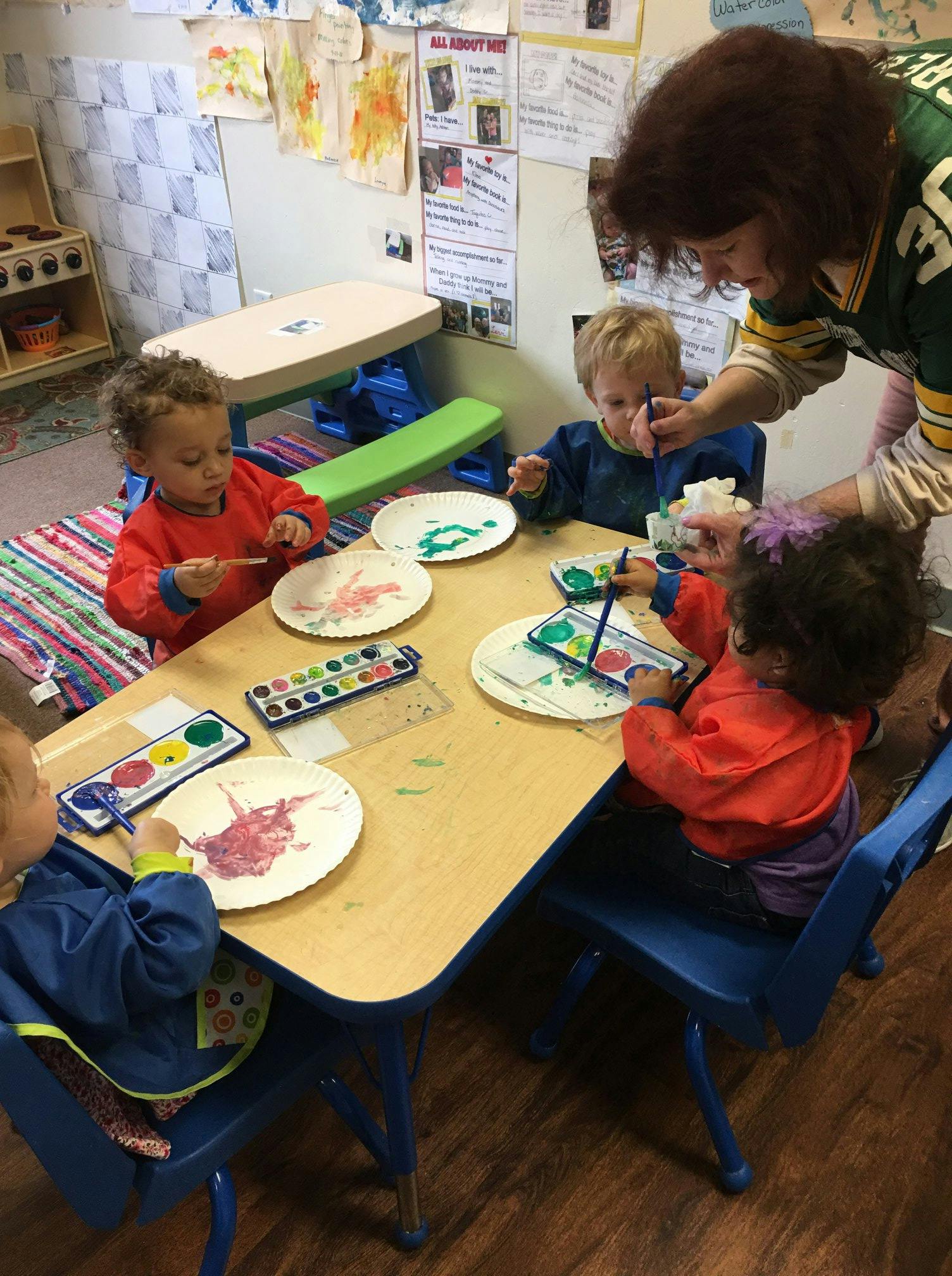 Adult and children painting at a table in a classroom