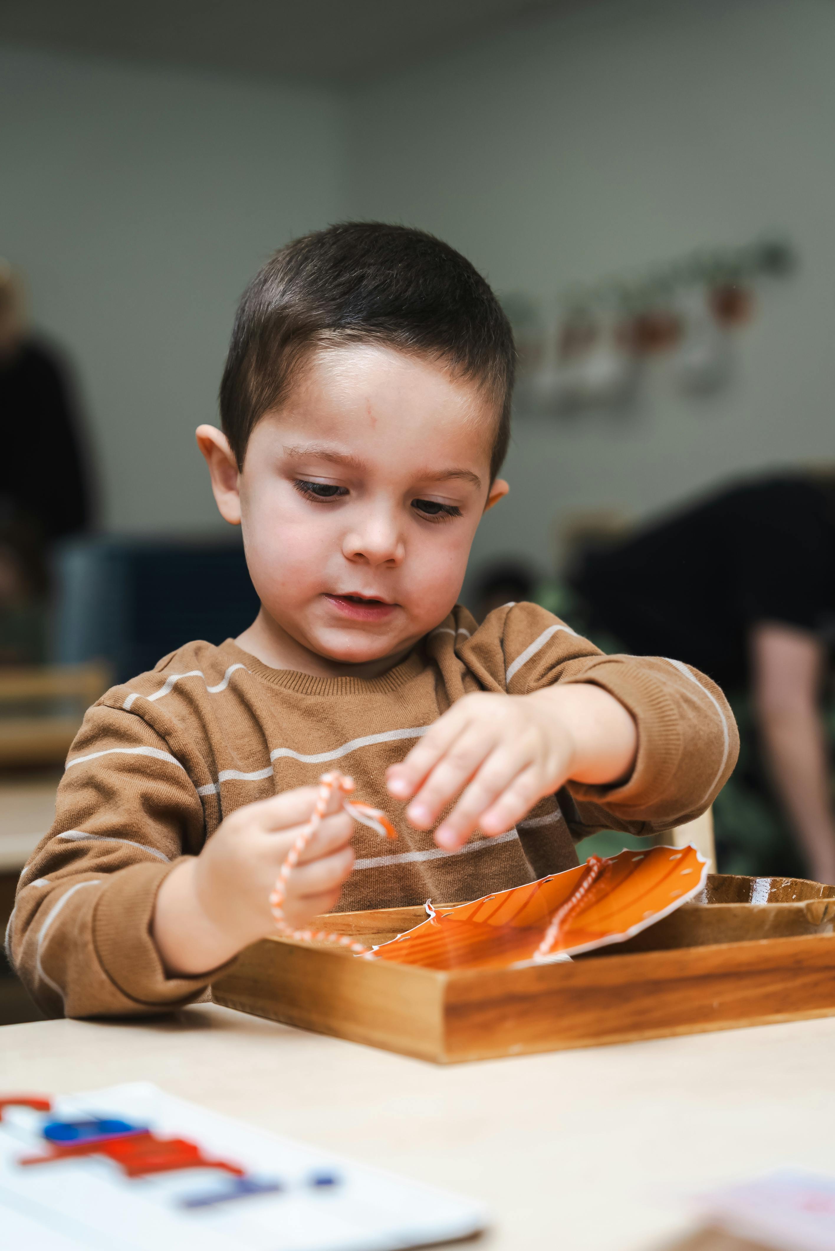 Child holding a string of beads over a wooden tray