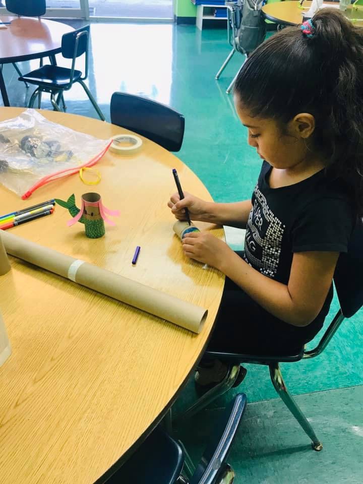 Child sitting at a table, drawing on a cardboard tube