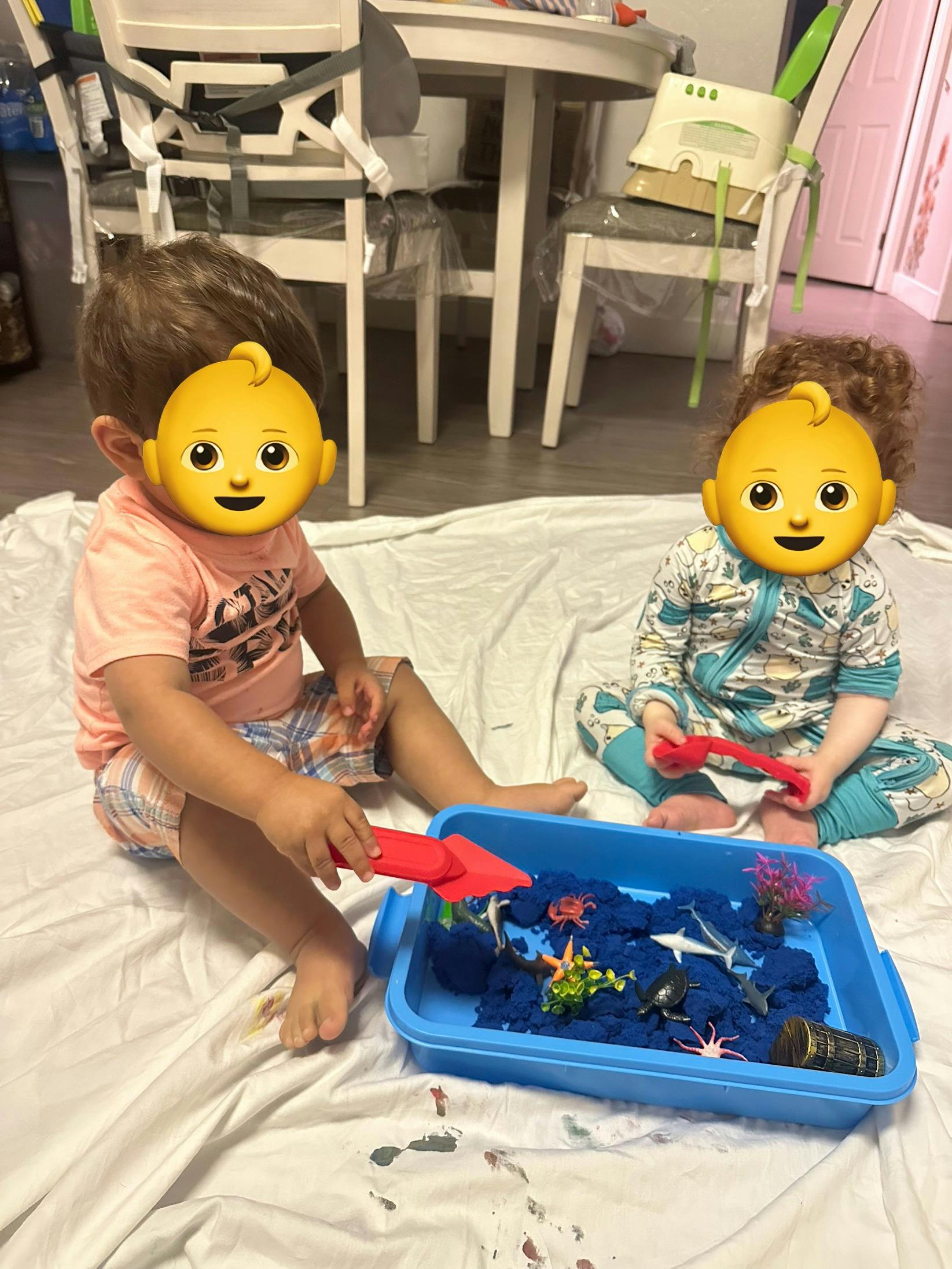 Two children playing with blue kinetic sand in a tray