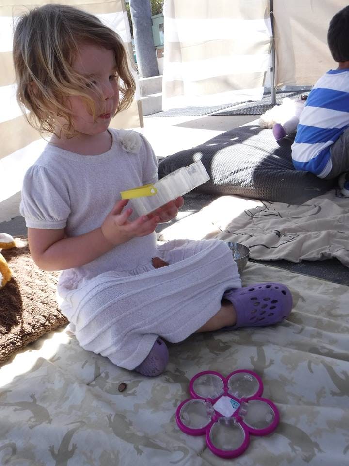 Child sitting on a blanket holding a small clear container
