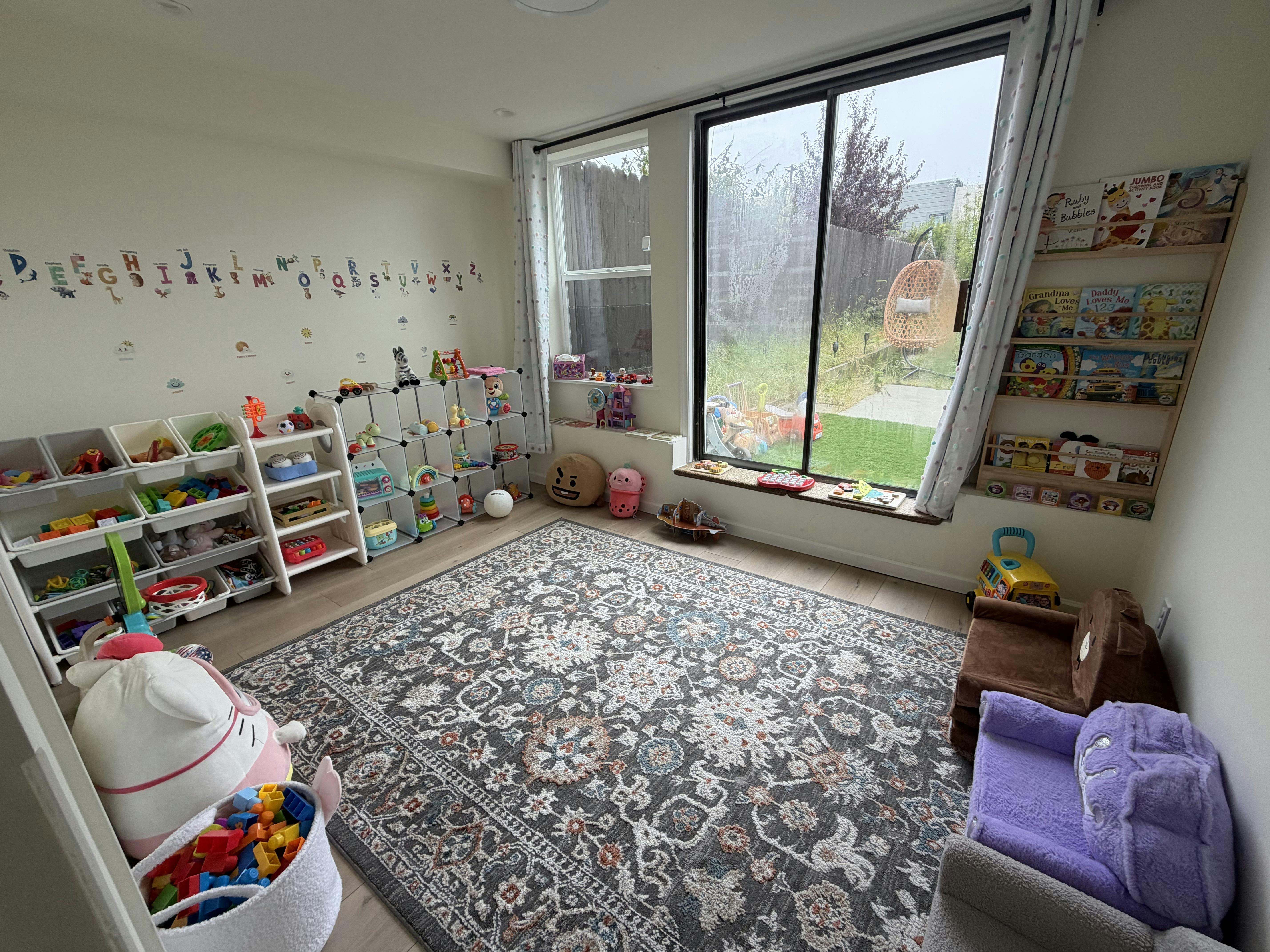 Playroom with alphabet decals on the wall, toy organizers, and a large patterned rug