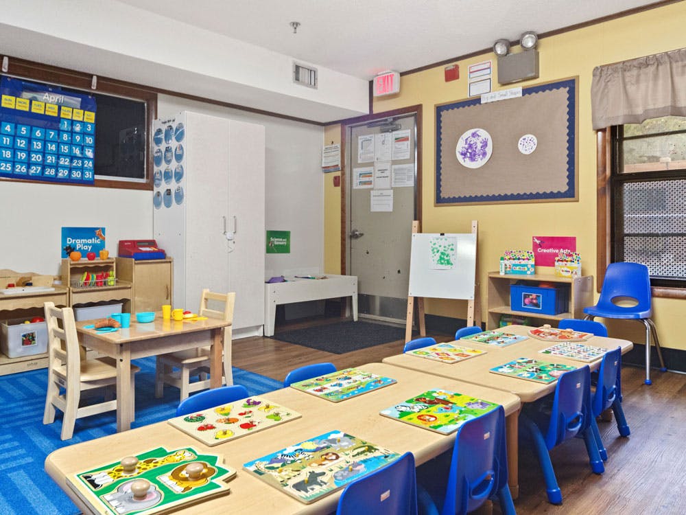 Classroom with small tables, blue chairs, puzzles, and a calendar on the wall