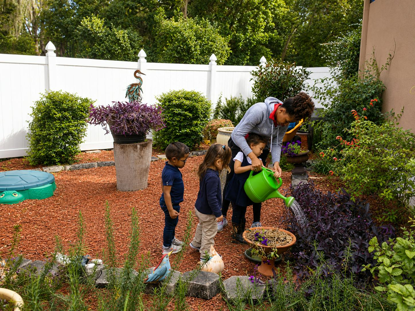 A person helping two children water a plant in a backyard