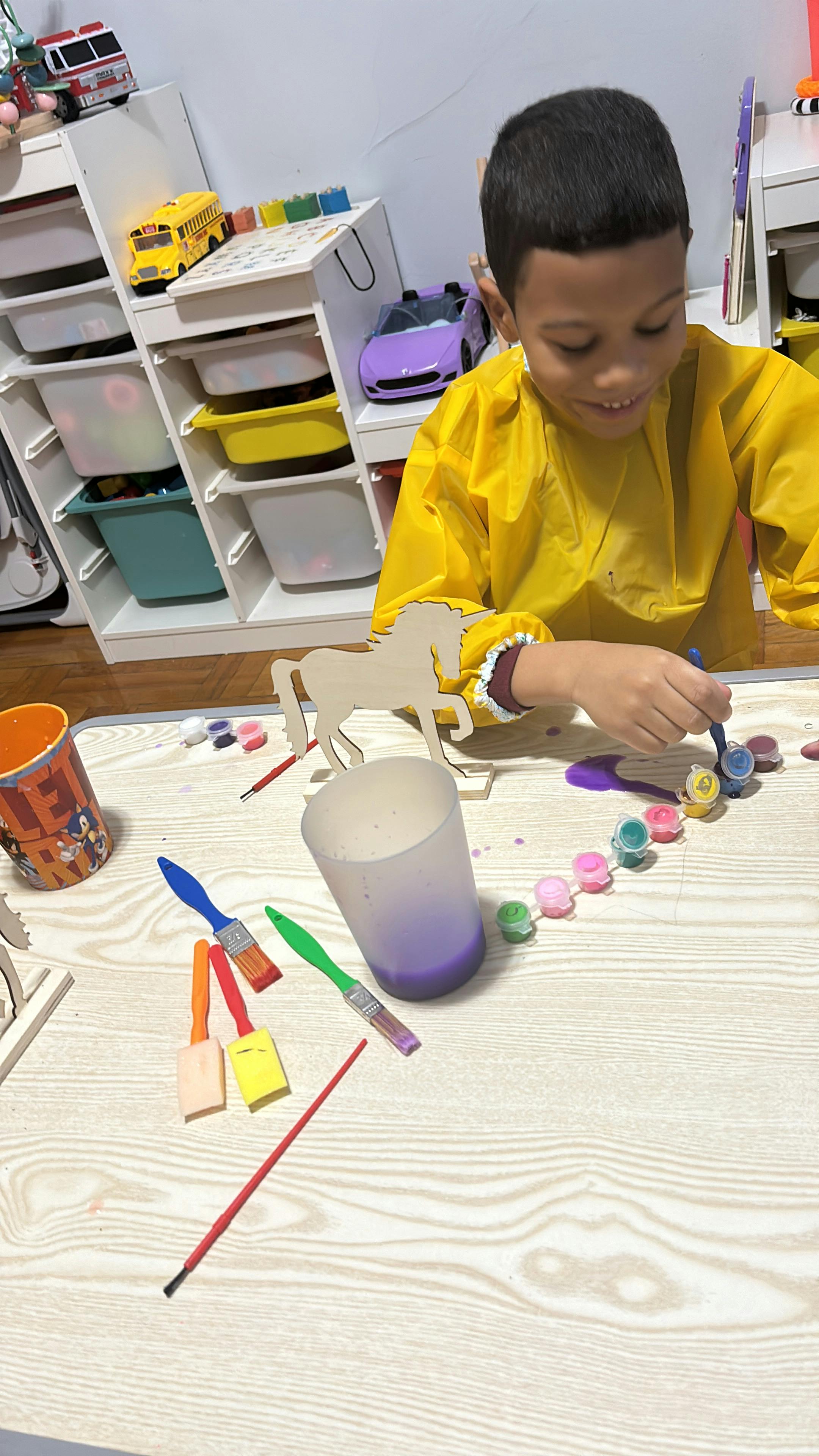 Child in yellow smock painting small objects on a table