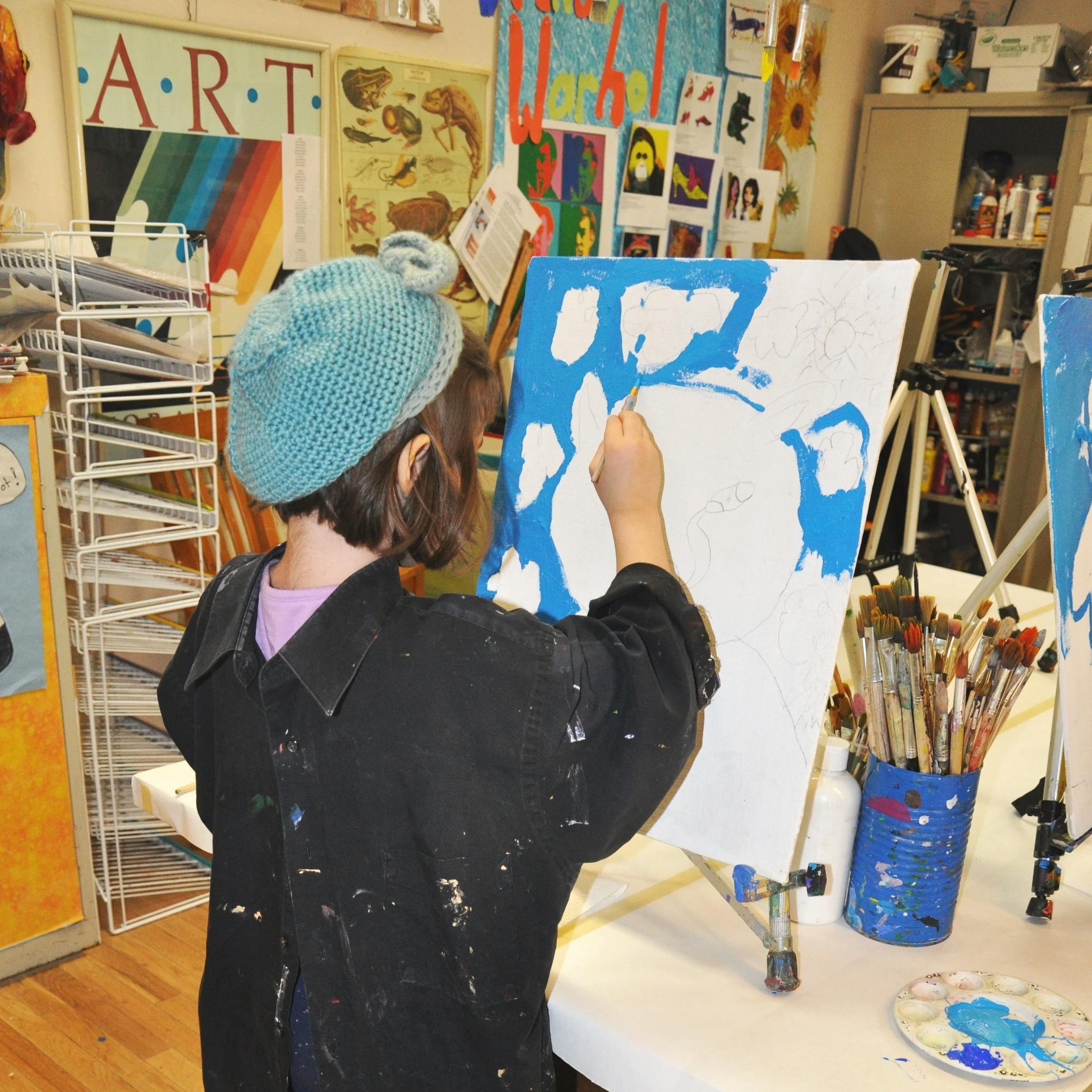 Child wearing a knitted hat painting on an easel in an art classroom