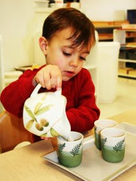 Child pouring from a small teapot into a cup