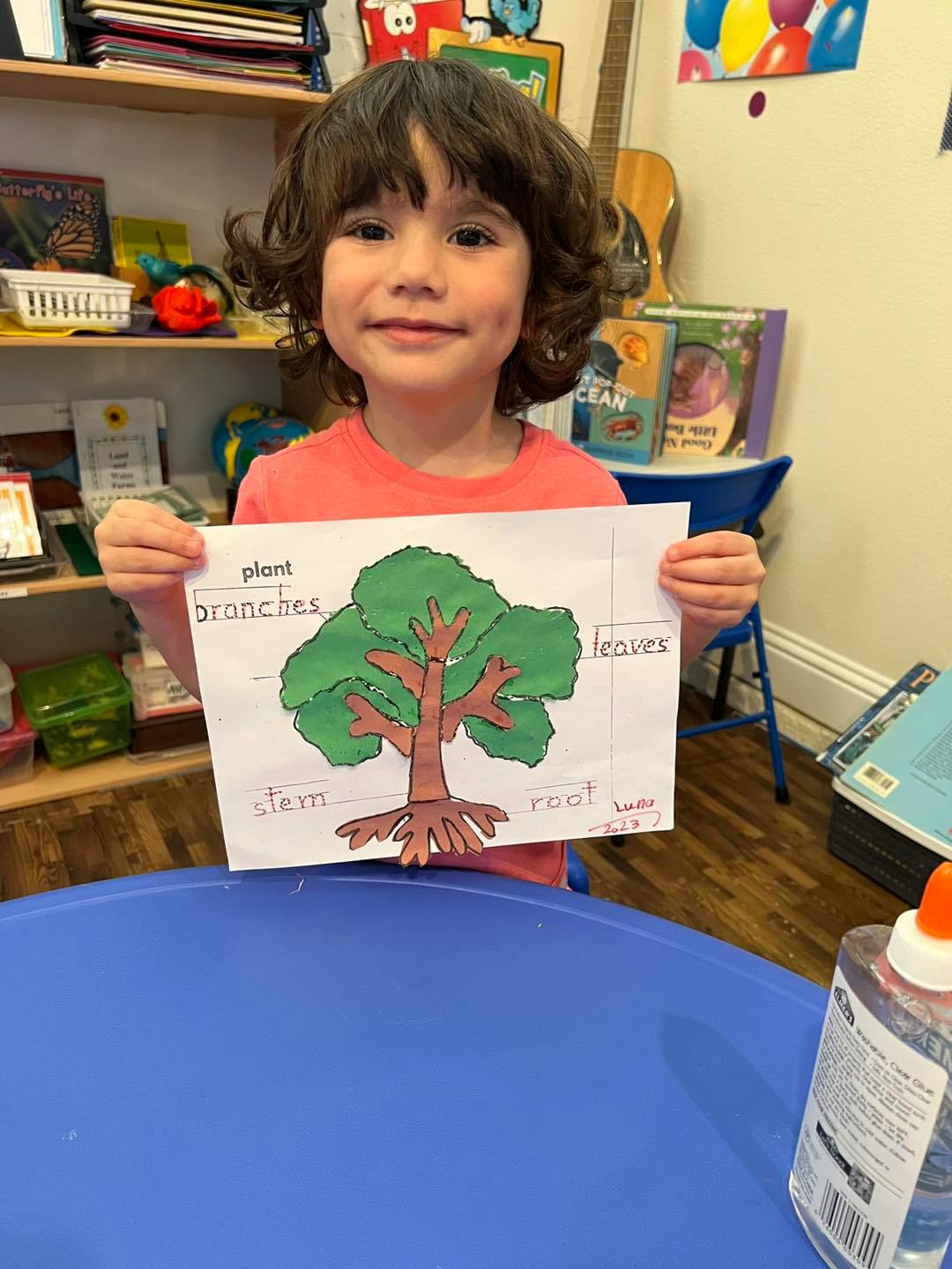 Child holding up a drawing of a tree with parts labeled