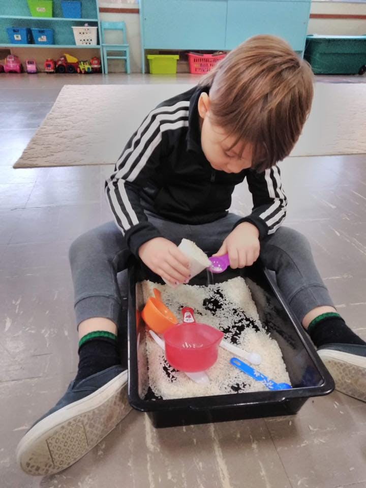 Child playing with rice and scoops in a sensory bin