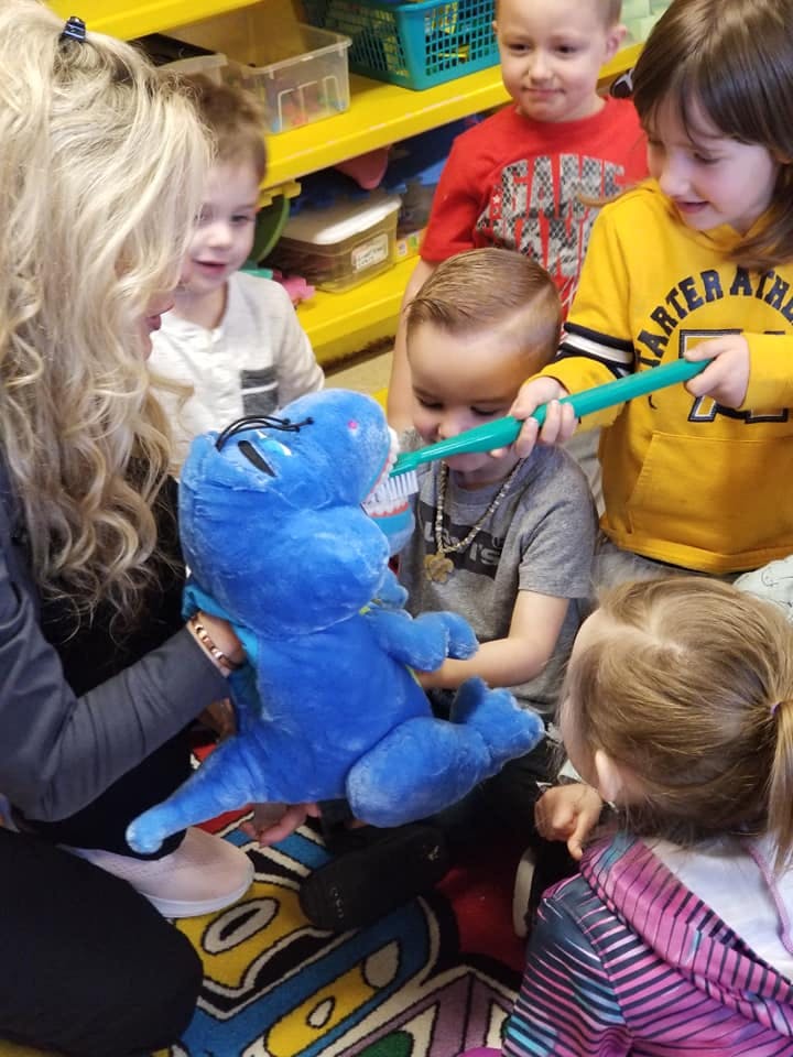 Adult and children brushing teeth of a blue stuffed animal