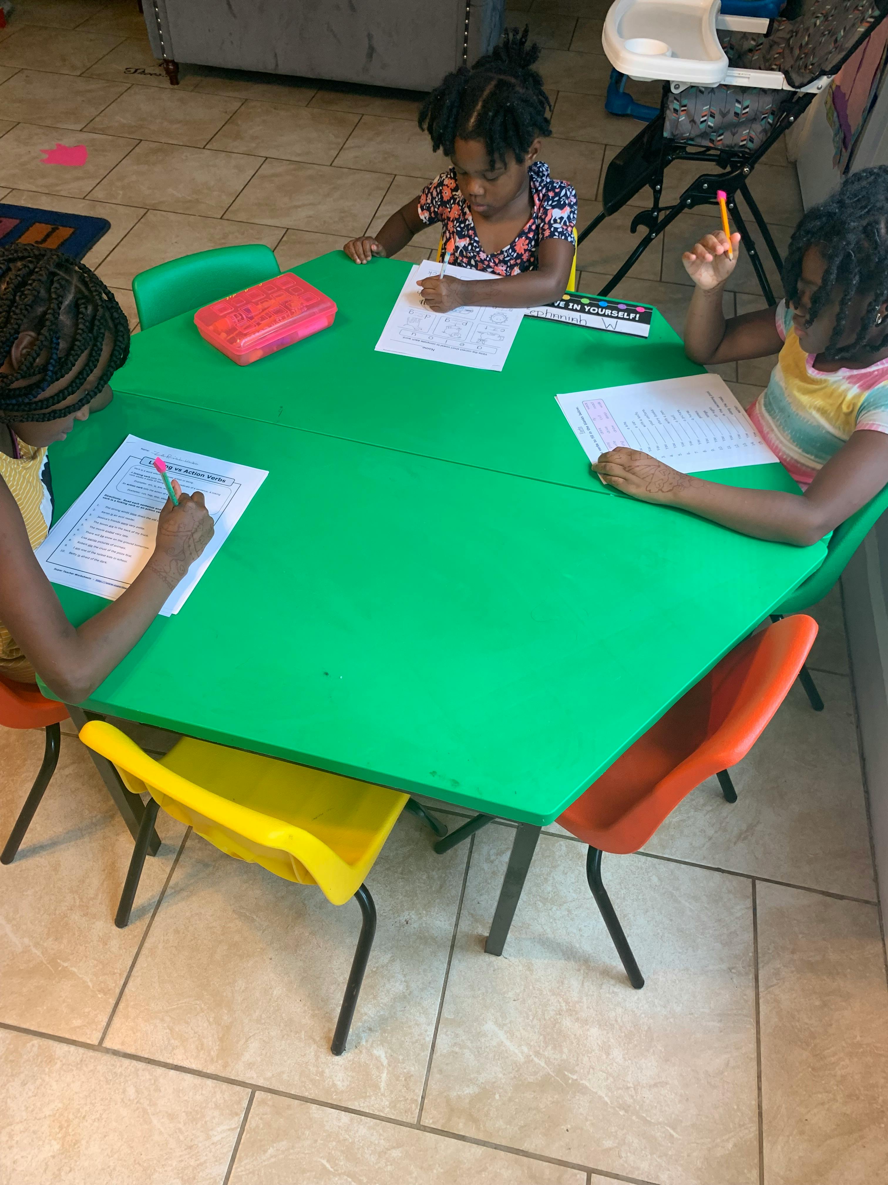 Three children sitting at a green table doing schoolwork