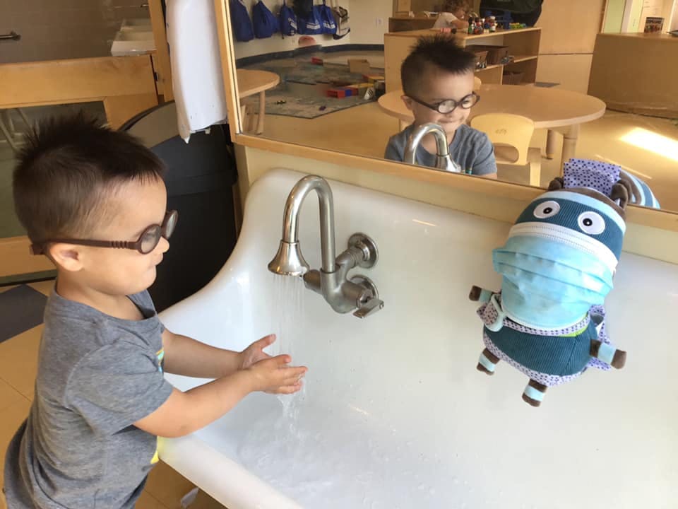 Child washing hands at a sink with a masked toy