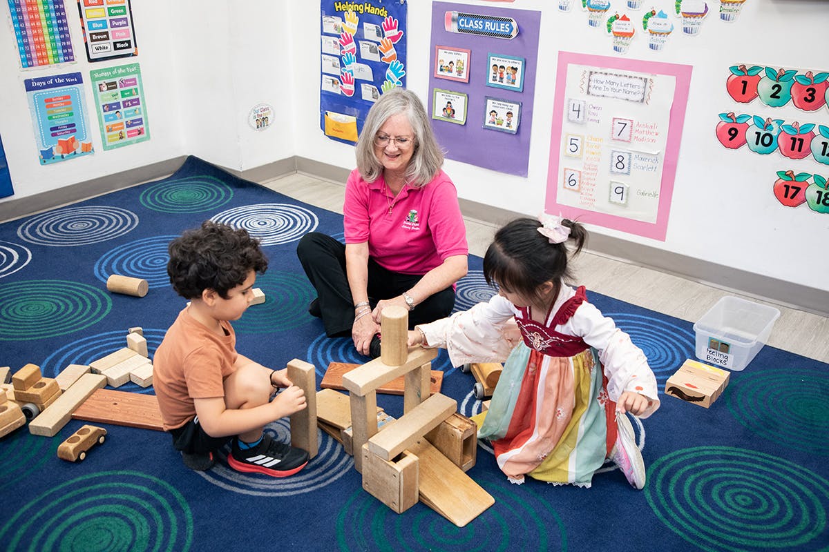 Adult and two children playing with wooden blocks in a classroom