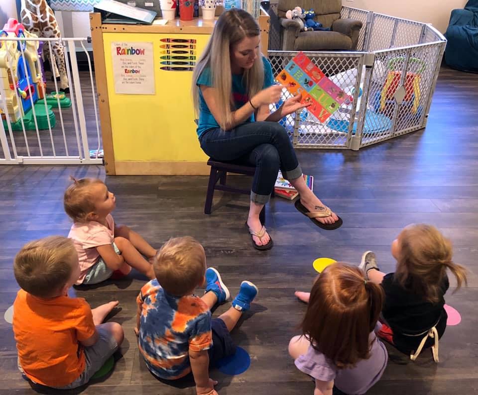 Person reading a book to a group of children sitting on the floor