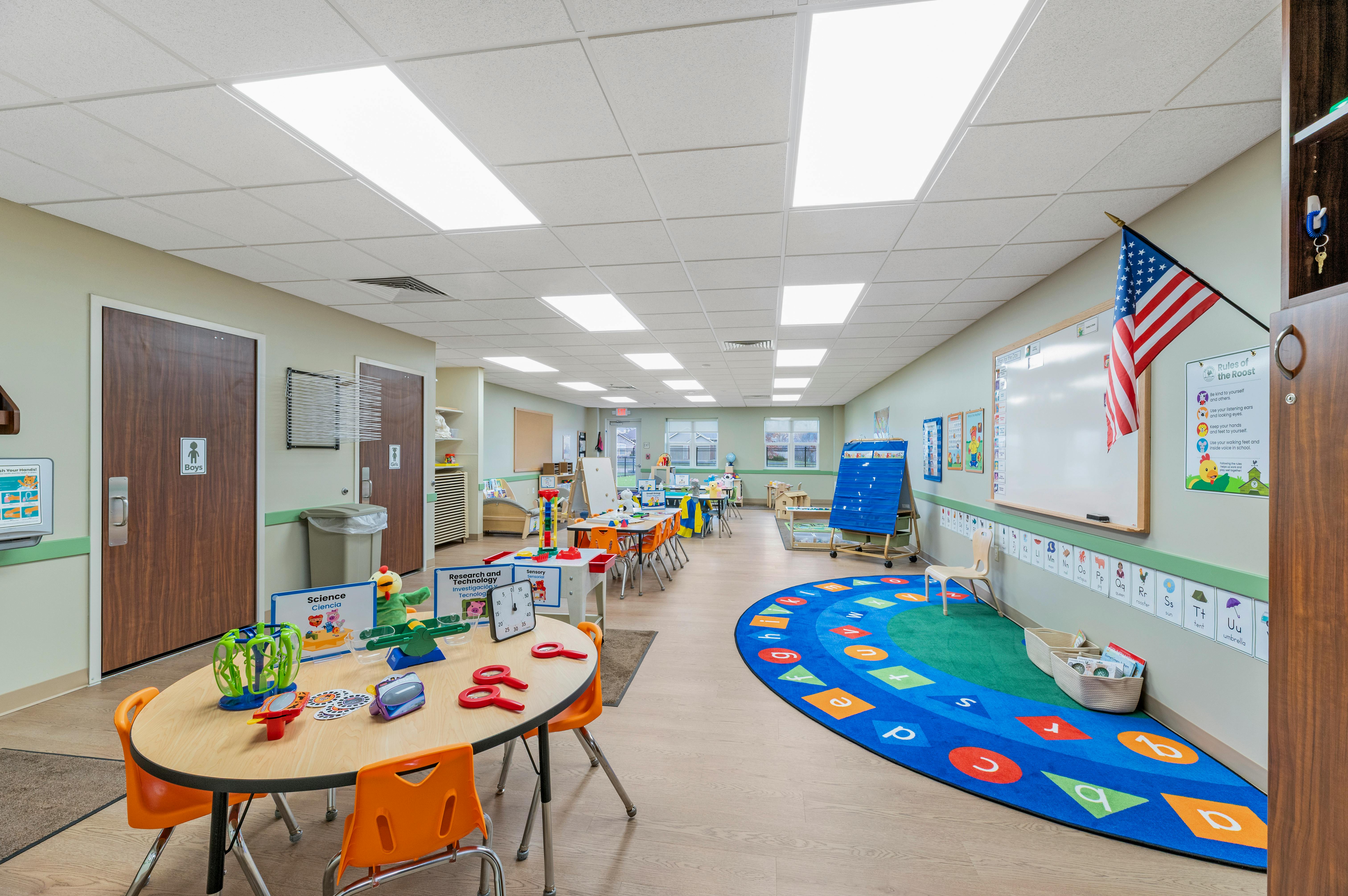 Classroom with small tables, chairs, and learning materials, an alphabet rug