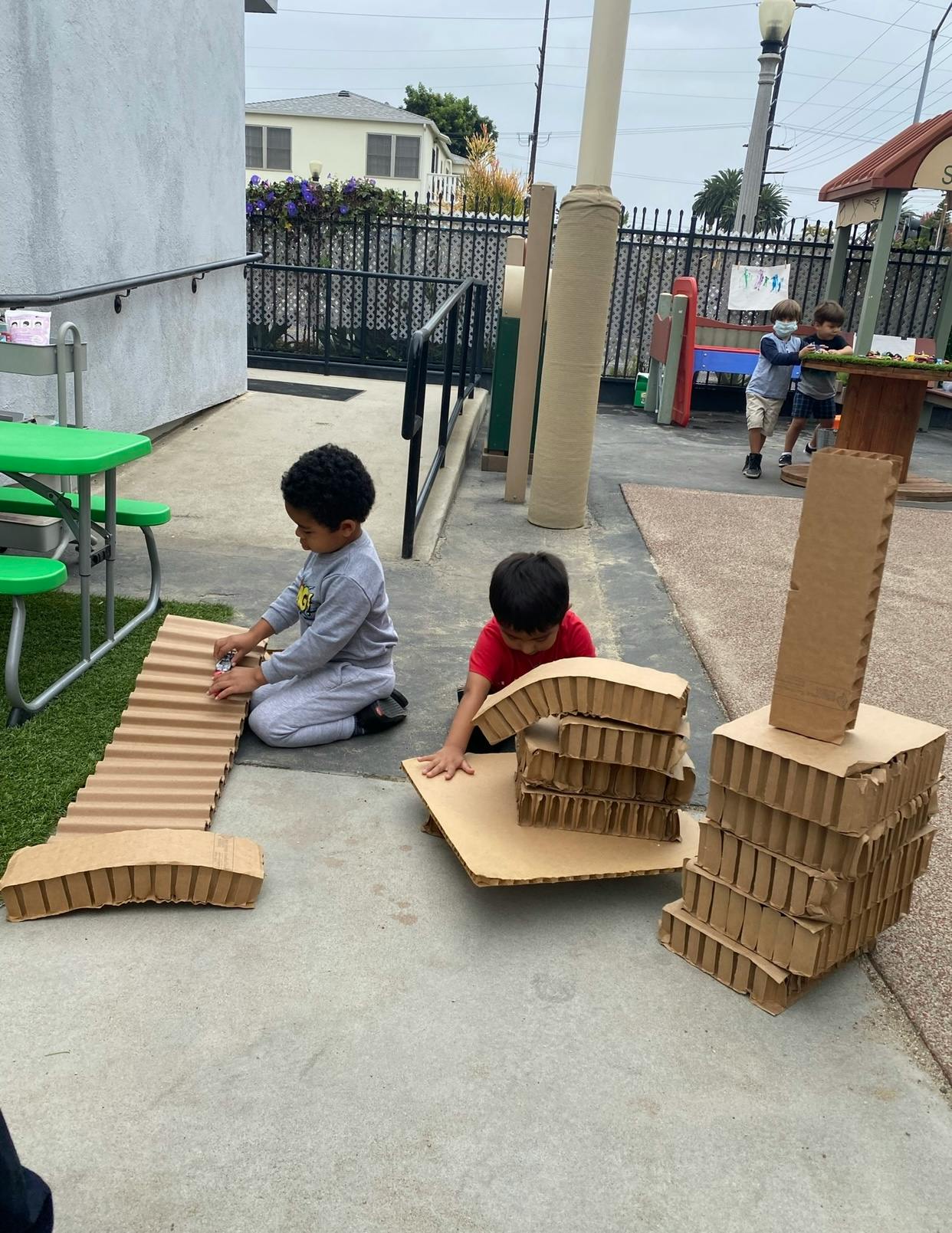 Two children playing with cardboard pieces outdoors