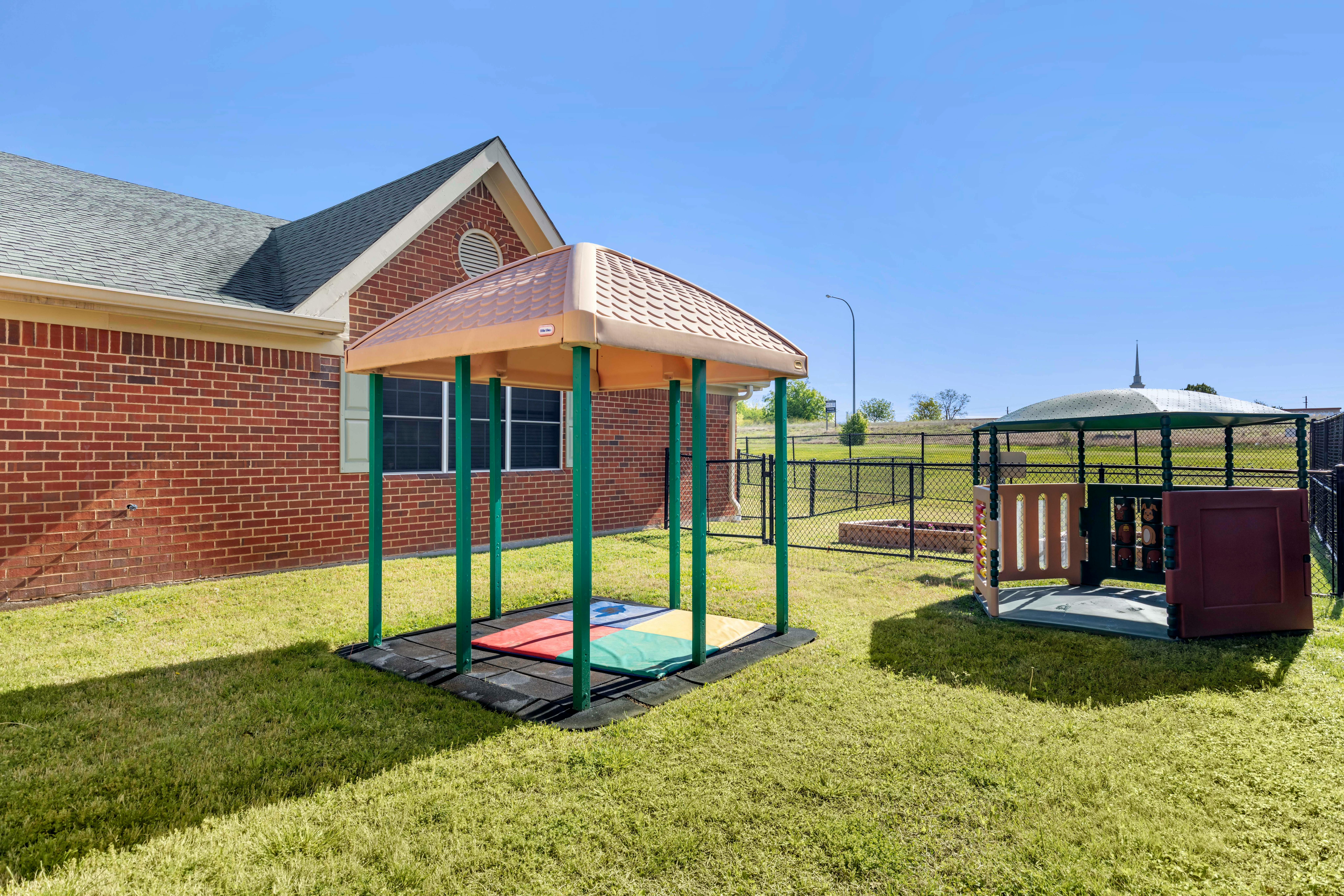 two play structures with canopies on a grassy area next to a brick building