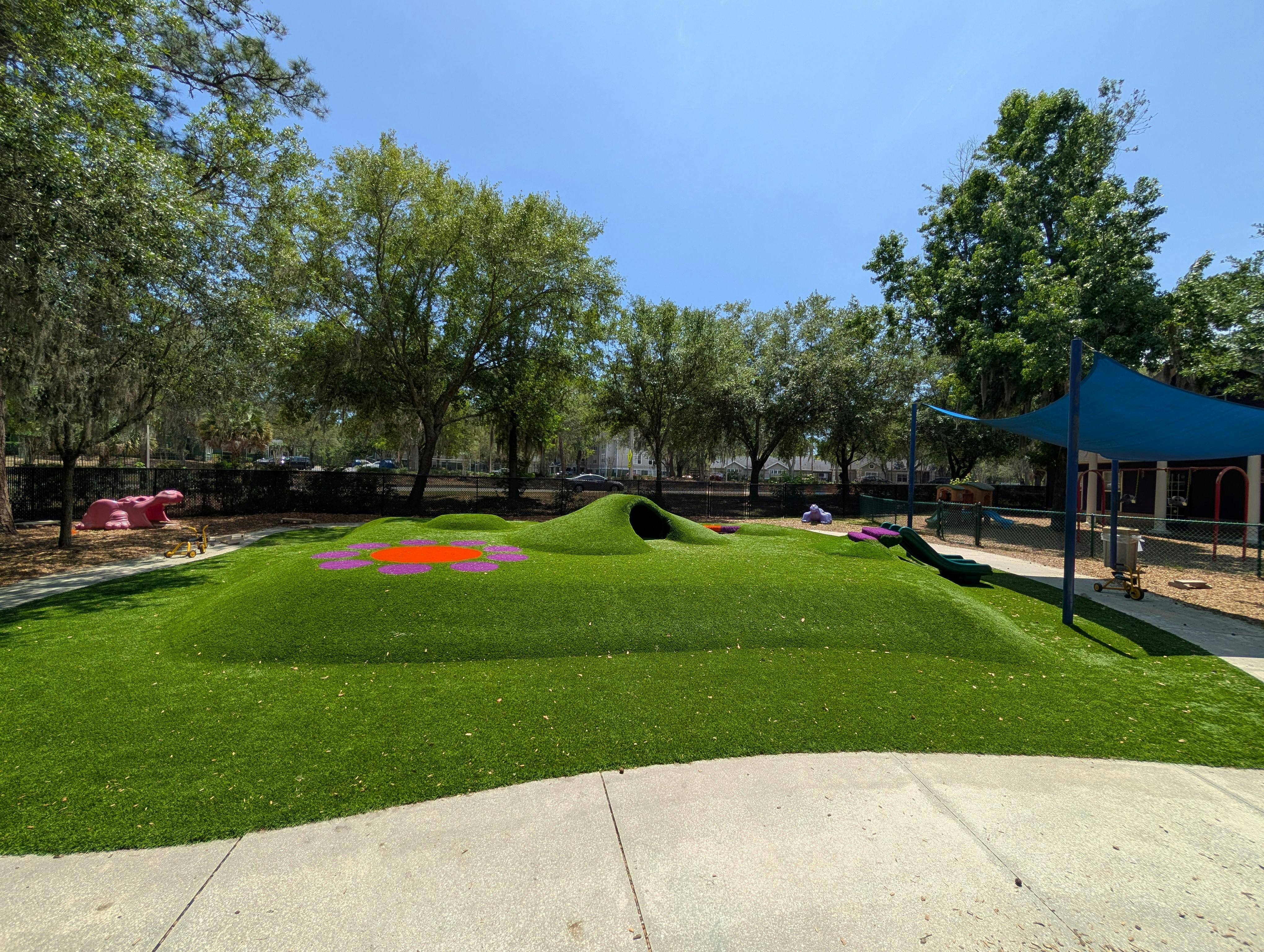 Playground with grassy hills, a pink hippopotamus statue, and a blue shade canopy