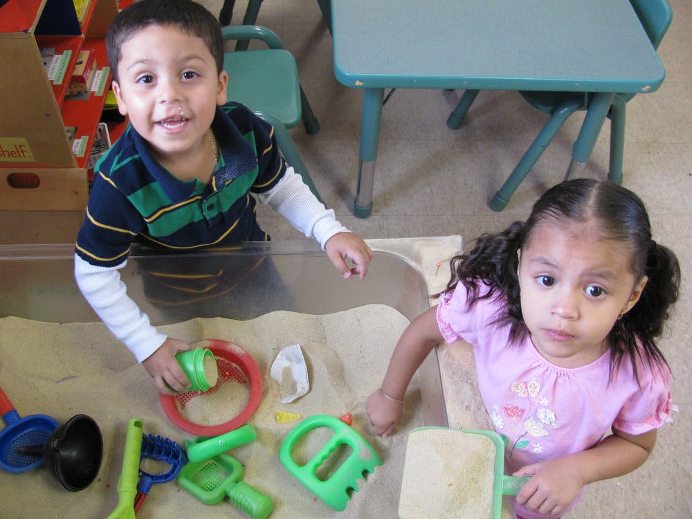 Two children playing in a sand table with toys