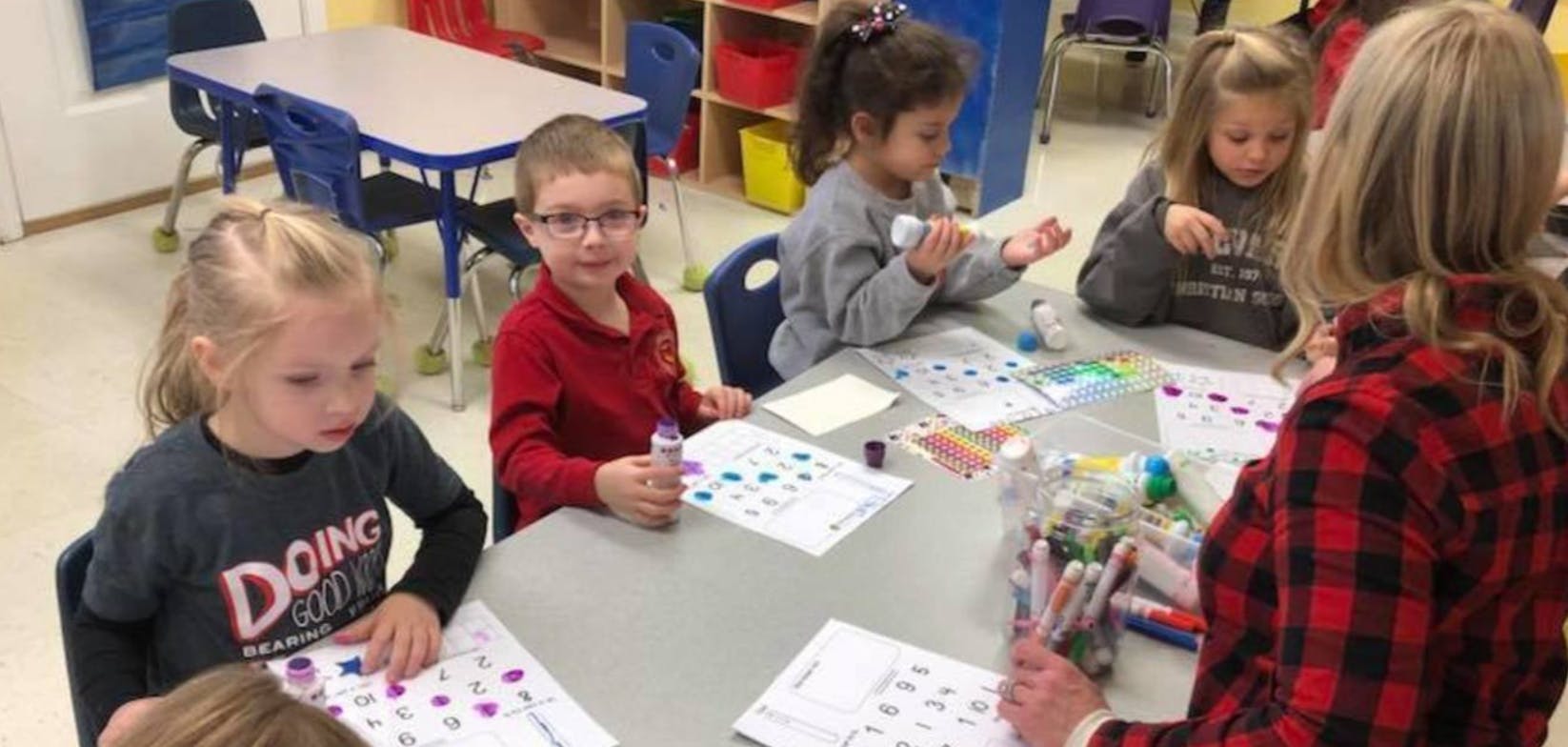 Children and an adult at a table with papers and craft supplies