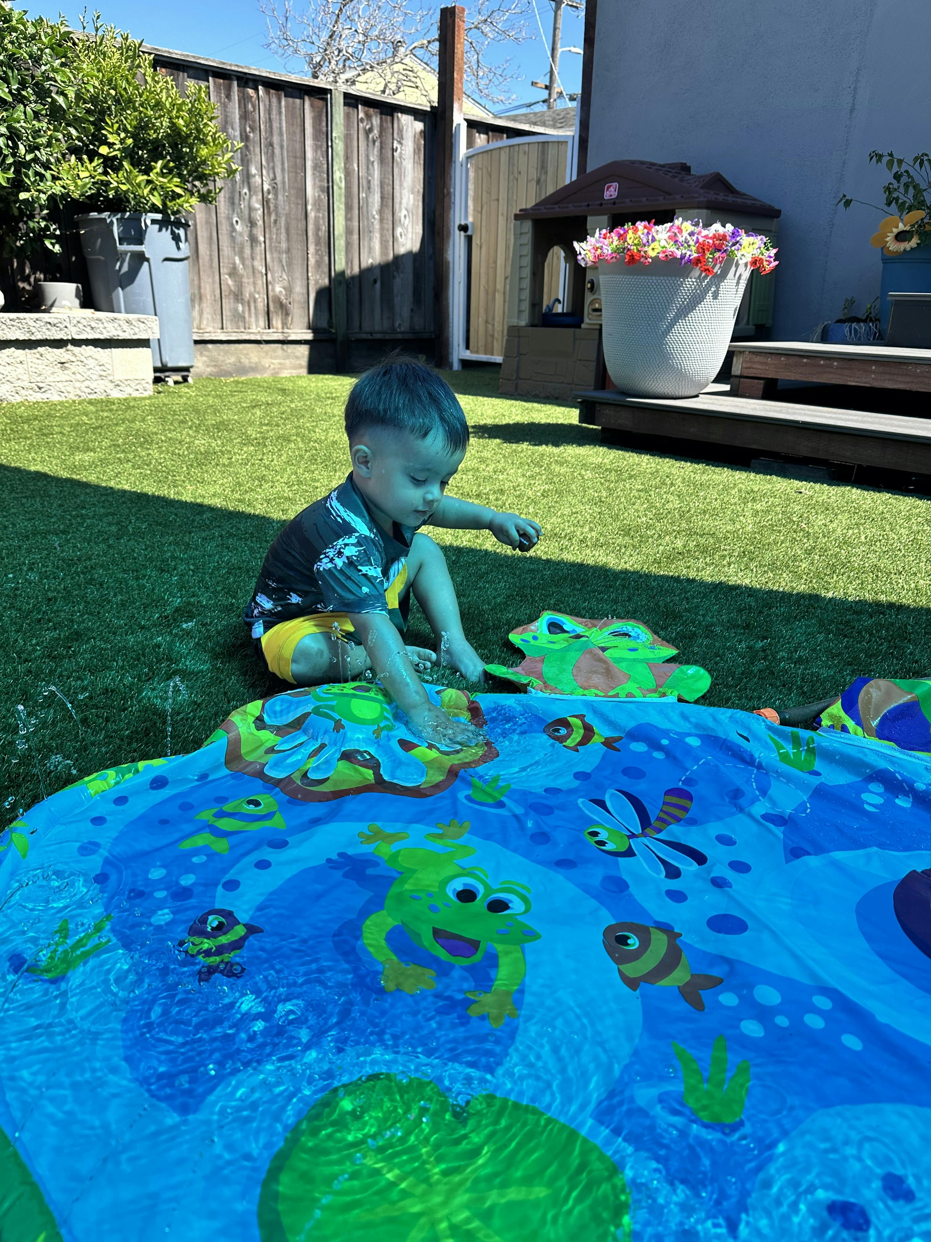 Child playing in a water splash mat on artificial grass in a backyard