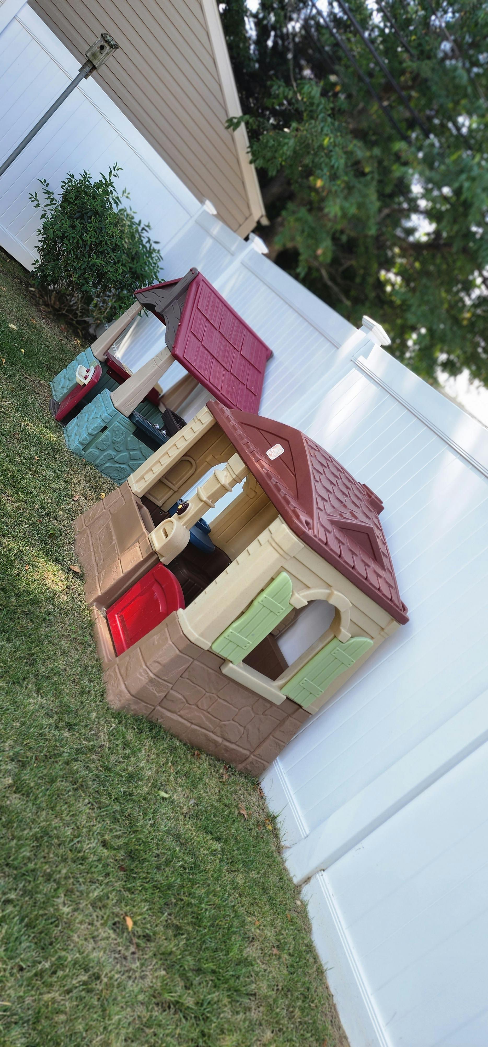 Two plastic playhouses on grass next to a white fence