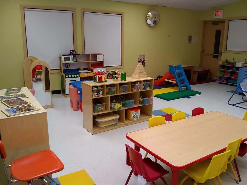 Classroom with play kitchen, storage shelves, and small tables with chairs