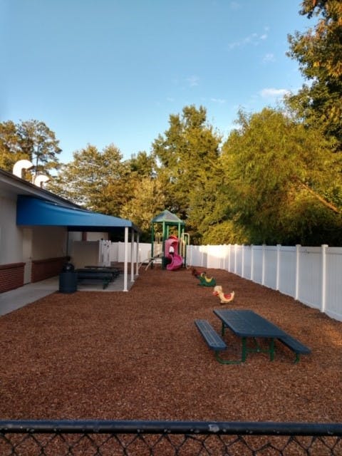 Outdoor playground with wood chips, picnic tables, and play equipment
