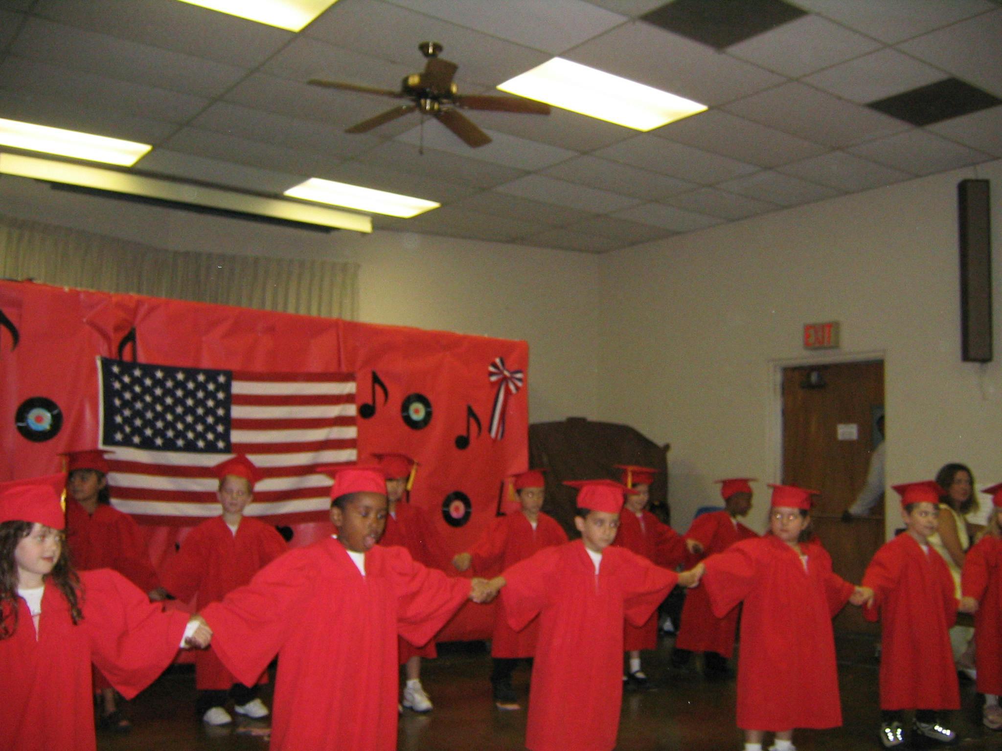 Children in red graduation gowns holding hands in a line